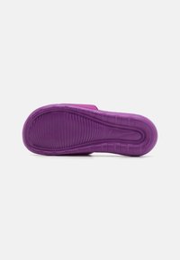 Semelle en caoutchouc violette avec des rainures texturées, présentant une zone lisse et légèrement surélevée ainsi qu'un bout arrondi. Logo Nike visible.