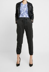 Czarne dresy z elastycznymi mankietami, dwoma przednimi kieszeniami, zestawione z niebieską koszulką tie-dye i czarną skórzaną kurtką. Czarne szpilki.