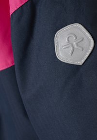 Tessuto esterno blu navy con una trama a spina di pesce, caratterizzato da una parte superiore rosa e un distintivo logo gommato grigio a forma esagonale.