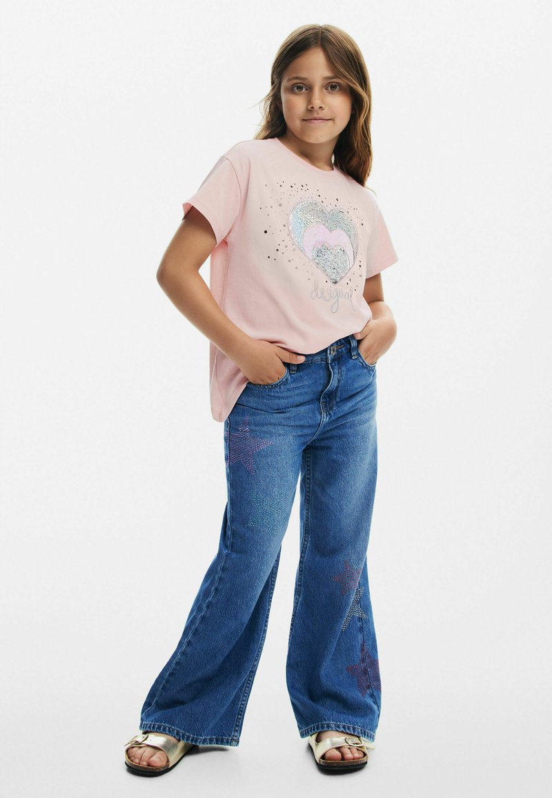 T-shirt rosa a maniche corte con grafica di cuore glitterato. Abbinato a jeans in denim blu a palazzo con motivi di stelle luccicanti. Sandali argentati.