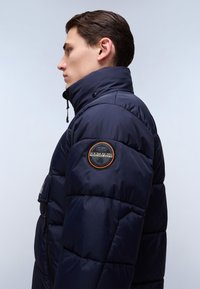 Námořnická puffer bunda s vysokým límcem, s logem na levém rukávu, prošívanou texturou, přední kapsou na zip a detaily na stažení.