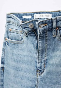 Jean en denim bleu clair avec braguette partiellement dézippée, bouton visible, poches avant et étiquettes de marque à l'intérieur de la ceinture.
