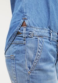 Světle modré džíny z denimu s vysokým pasem, postranními kapsami a prošíváním podél švů. Měkká textura s mírně opotřebovaným vzhledem.