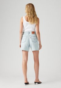 Lichtblauwe denimshorts met rechte snit, rafelige zoom en achterzakken; gecombineerd met een wit tanktop en zwarte sandalen.
