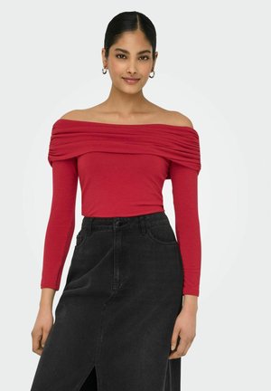 Rød off-the-shoulder top med lange ærmer, der har plisseret design. Parret med en højhalset sort denimnederdel med en slids foran.