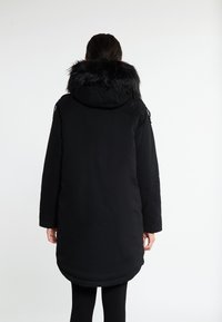 Sort parka med en faux fur hætte. Lange ærmer, lige snit og sidelommer. Glat tekstur, knælangt design.