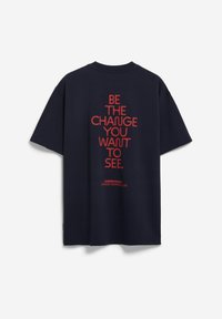 T-shirt en coton bleu marine à manches courtes ; présente un texte rouge vif au dos : "SOYEZ LE CHANGEMENT QUE VOUS VOULEZ VOIR." Comprend un détail de marque.