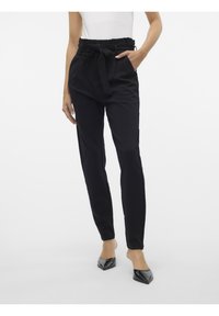 Pantalons noirs ajustés avec une taille haute, un détail de lien à l'avant, et des poches sur les côtés ; tissu lisse avec une silhouette épurée ; accompagnés de talons brillants.