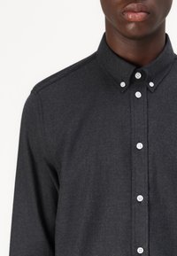 Donkergrijs button-up shirt met een kraag, lange mouwen en witte knopen. Heeft een gestructureerde stof en een getailleerd ontwerp.