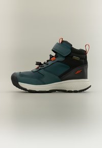 Παιδικό παπούτσι μεσαίου ύψους σε σκούρο πετρόλ και μαύρο με αδιάβροχο υλικό, πορτοκαλί λεπτομέρειες, λουράκι με βέλκρο και υφή στις πλευρικές επιφάνειες. Λευκή εξωτερική σόλα.