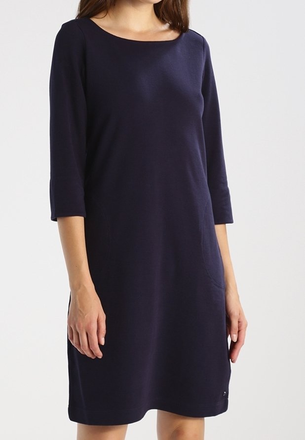 Femme portant une robe simple bleu marine à mi-genoux avec des manches trois-quarts et un décolleté bateau.