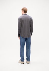 Grå långärmad skjorta med krage, sammansatt med blå jeans och beige sneakers. Skjortan har en något rundad nederkant och knäppte manschetter.