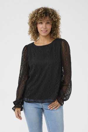 Black lace blouse with long, puffed sleeves, featuring geometric patterns and a round neckline. Worn over light blue fitted jeans.