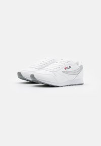 Chaussures de sport blanches avec une tige en cuir lisse, des accents gris, un bout arrondi et des semelles en caoutchouc texturées. Dotées de lacets et du logo de la marque.