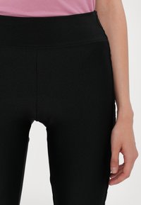 Leggings neri realizzati in un tessuto morbido e elastico. Vita alta e design aderente, con pannelli laterali e finitura opaca.
