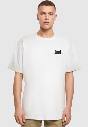 White cotton t-shirt with a loose fit, featuring a small black cat graphic on the left chest pocket area. Short sleeves, round neckline.