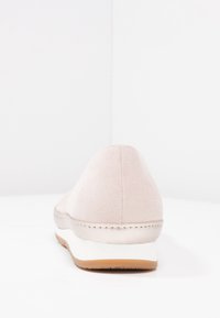 Světle růžové semišové tenisky s zaoblenou zadní částí, bílou mezipodešví a hnědou podešví. Jednoduchý design bez viditelných vzorů nebo ozdob.