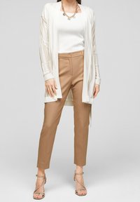 Lekka, kremowa kardigan na dopasowanej białej bluzce, zestawiona z beżowymi spodniami i paskowymi beżowymi sandałami; warstwowe faktury i neutralne kolory.