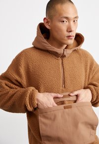 Hoodie castanho em fleeced com gola com zíper, bolso frontal e punhos elásticos. Tecido texturado e aconchegante com forro liso na capuz e pormenores.
