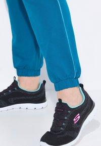 Blå joggers med elastiska muddars i nederkant, kombinerade med svarta sportskor med turkosa accenter och flexibla vita sulor.