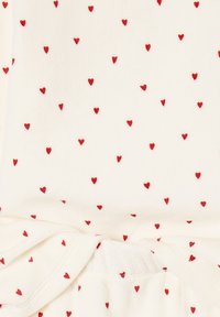 White fabric with small red heart patterns, featuring a tie detail at the waist. Soft texture with a smooth finish.