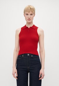 Rød ribbet ermeløs polo topp med en tettsittende design, som har krage og knappestolpe, parret med mørk denim jeans.