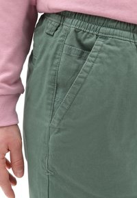 Pantalones de algodón verde claro con cintura elástica y bolsillos laterales, con costuras planas y una textura suave.
