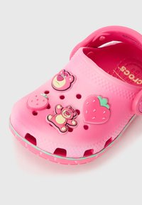 Zoccoli in gomma rosa con decorazioni di personaggi e fragole, dotati di fori di ventilazione e una suola di un blu chiaro a contrasto.
