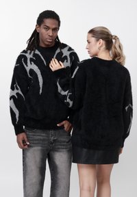 Črn in siv veliki pulover z puhasto teksturo in abstraktnim vzorcem, kombiniran s svetlo sivimi kavbojkami in črno usnjeno mini krilo.