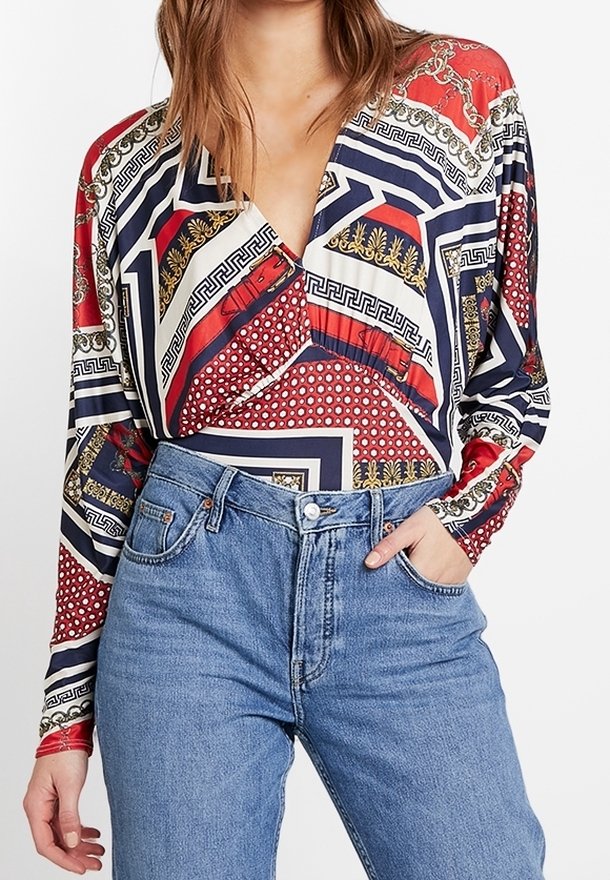Langærmet bluse med en dyb V-udskæring, prydet med geometriske mønstre i rød, marineblå og guld på et glat stof. Matcher med højtaljede jeans.
