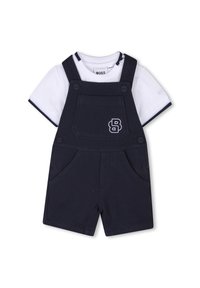 Navy blue cotton overalls with suspenders, featuring a front pocket and side pockets. White t-shirt underneath has navy trim and logo.