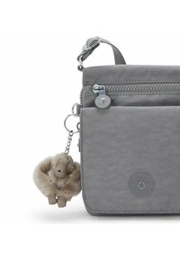 Bolsa sintética gris con múltiples bolsillos con cremallera, que presenta un logo redondo y un llavero de un mono de peluche beige adjunto a un clip de metal.