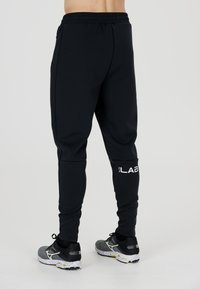 Sorte sweatpants med slim fit, elastisk talje, sidelommer og hvidt logo på venstre læg. Blødt bomuldsblandingsmateriale.
