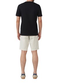Czarna koszulka z krótkim rękawem, zestawiona z jasnobeżowymi szortami, widok z tyłu. Wygodne obuwie dopełnia stylizację.