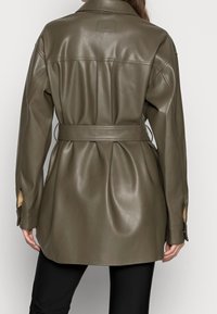 Giacca in pelle verde oliva con cintura, vestibilità ampia, polsini abbottonati e texture liscia. Presenta uno yoke posteriore per maggiore struttura.