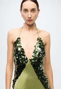 Green sequin halter dress with a deep V-neckline, fitted shape, and smooth satin fabric. Features shiny round sequins arranged in patterns.