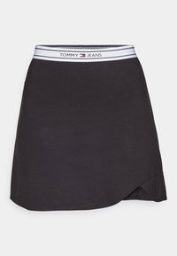 Musta hame, jossa on istuva vyötärönauha ja "TOMMY JEANS" -brändäys. Siinä on hienovarainen kietaisumallinen muotoilu ja sileä, joustava materiaali.