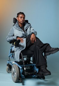 Šviesiai mėlynas pūkuotas paltas su dideliu gobtuvu, juodų juostų marškiniai ir plačios juodos kelnės. Juodas vežimėlis su vidutinio profilio ratais ir tamsi avalynė.