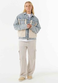 Denimjakke med fleece foran, lyseblå og creme farver. Kombineret med beige teksturerede cargo bukser og slip-on fodtøj.
