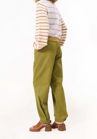 Olivově zelené široké kalhoty s vysokým pasem a ohrnutými nohavicemi, doplněné pruhovaným svetr s pastelovými barvami. Hnědé sandály na blokovém podpatku.