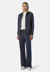 Felpa con zip di colore navy con cappuccio regolabile, abbinata a pantaloni a gamba larga; entrambi realizzati in materiale morbido, con un semplice logo decorativo.