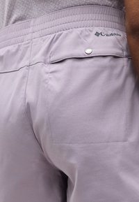 Κοντινό πλάνο ενός ατόμου που φοράει ανοιχτό μοβ σορτς Columbia με ελαστική μέση και πίσω τσέπη με κουμπί τύπου snap.