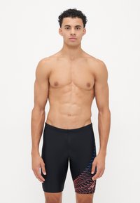 Fekete fürdőshorts, testhez simuló fazonnal. Bal lábon többszínű absztrakt minta látható vörös és kék színekben, elasztikus anyagból készült.