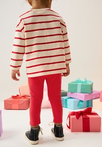 Maglietta a maniche lunghe a strisce rosse e bianche abbinata a leggings rossi e scarpe alte nere; scatole regalo colorate sullo sfondo.