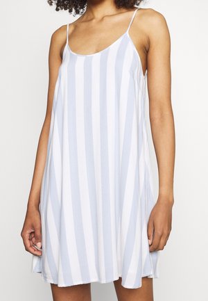 Femme portant une robe sans manches, ample, avec des rayures verticales blanches et bleu clair et de fines bretelles.