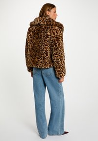 Giacca in pelliccia sintetica con stampa leopardata, colletto ampio, design corto e superficie texturizzata, abbinata a jeans in denim blu a vita alta.