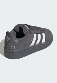 Mustat nupukkinahan urheilukengät, joissa on valkoinen kolmi-raitojen design, kumipohja ja pyöreä korko. Ominaisuuksiin kuuluu teksturoidut kieli ja logoelementti kantapäässä.