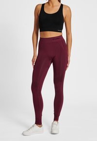 Leggings granate con cintura alta y detalles texturizados, combinados con un sujetador deportivo negro. El calzado son zapatillas deportivas blancas.