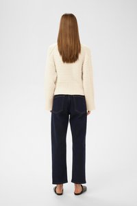 Kreemist ribatreeritud kampsunist, millel on mugav lõige, koos tumehallide sirgete pükstega. Lihtsad mustad jalanõud täiendavad riietust.