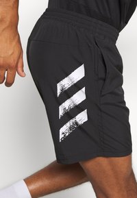 Pantalones cortos deportivos negros con una tela texturizada, cinturilla elástica y tres rayas gráficas blancas en el lateral.